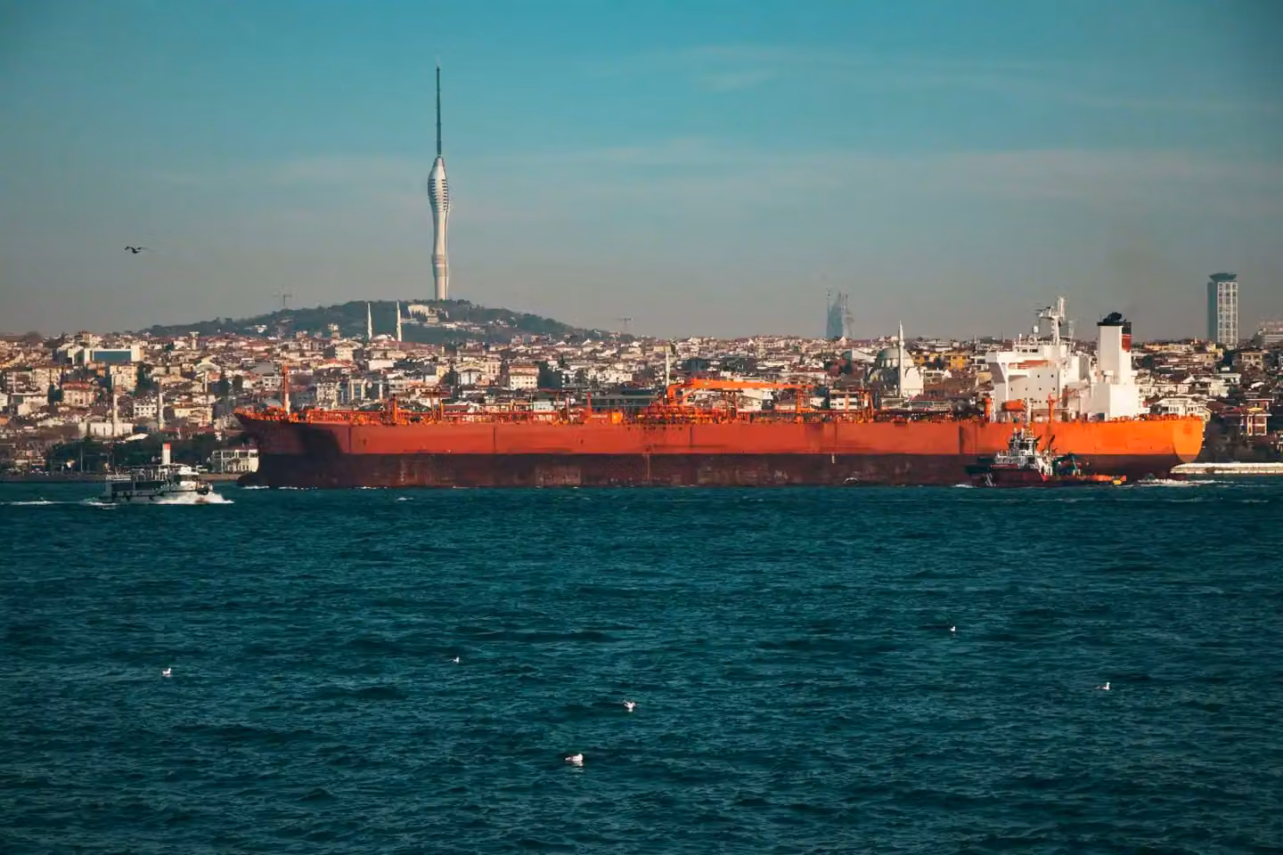 A large oil tanker navigates the Bosphorus Strait with Istanbul's skyline and Camlica Tower in the background.
