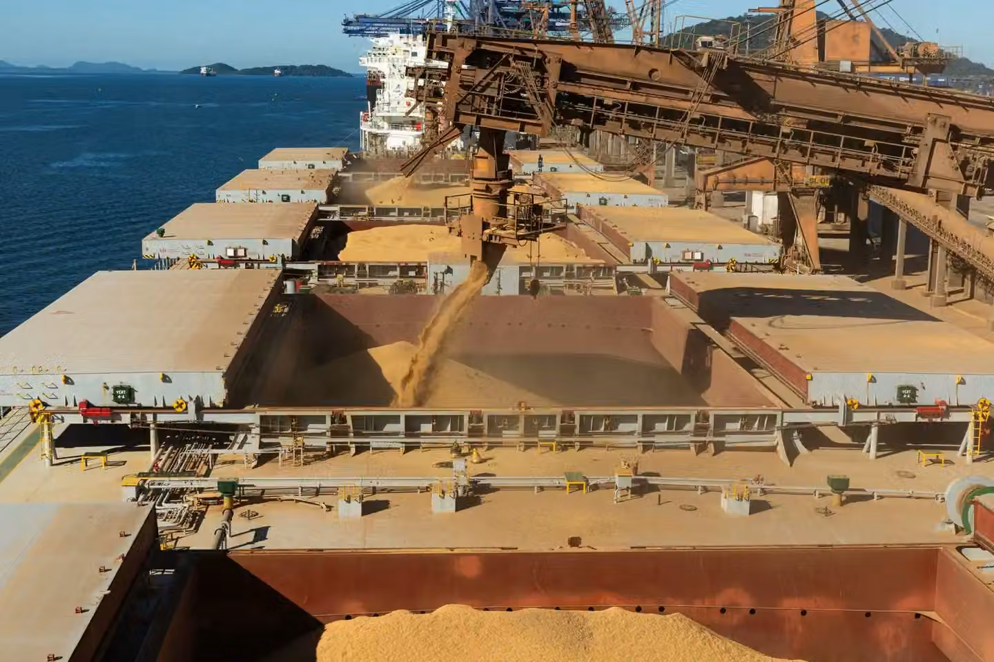 Aerial view of a cargo ship loading grain at a bustling industrial port by the sea.