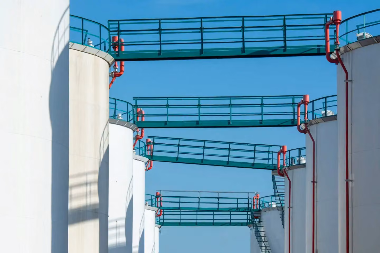 Modern industrial storage tanks with walkways against a clear blue sky.