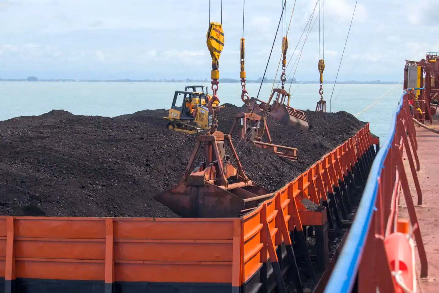 Heavy machinery loading coal onto a cargo ship at a seaport with cranes.