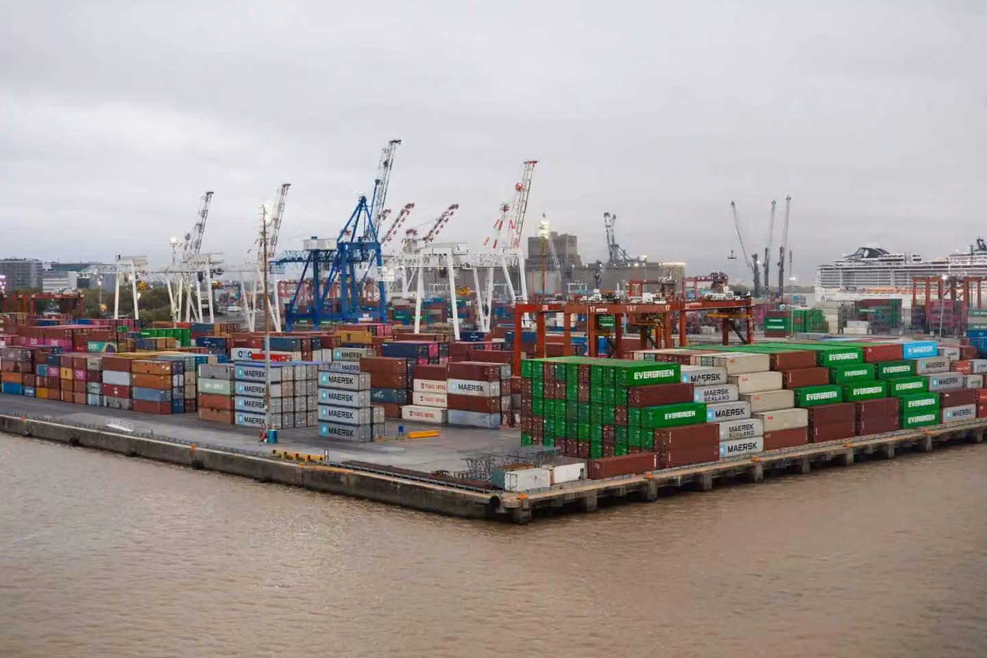 A bustling shipping port with stacked cargo containers and cranes under overcast skies.