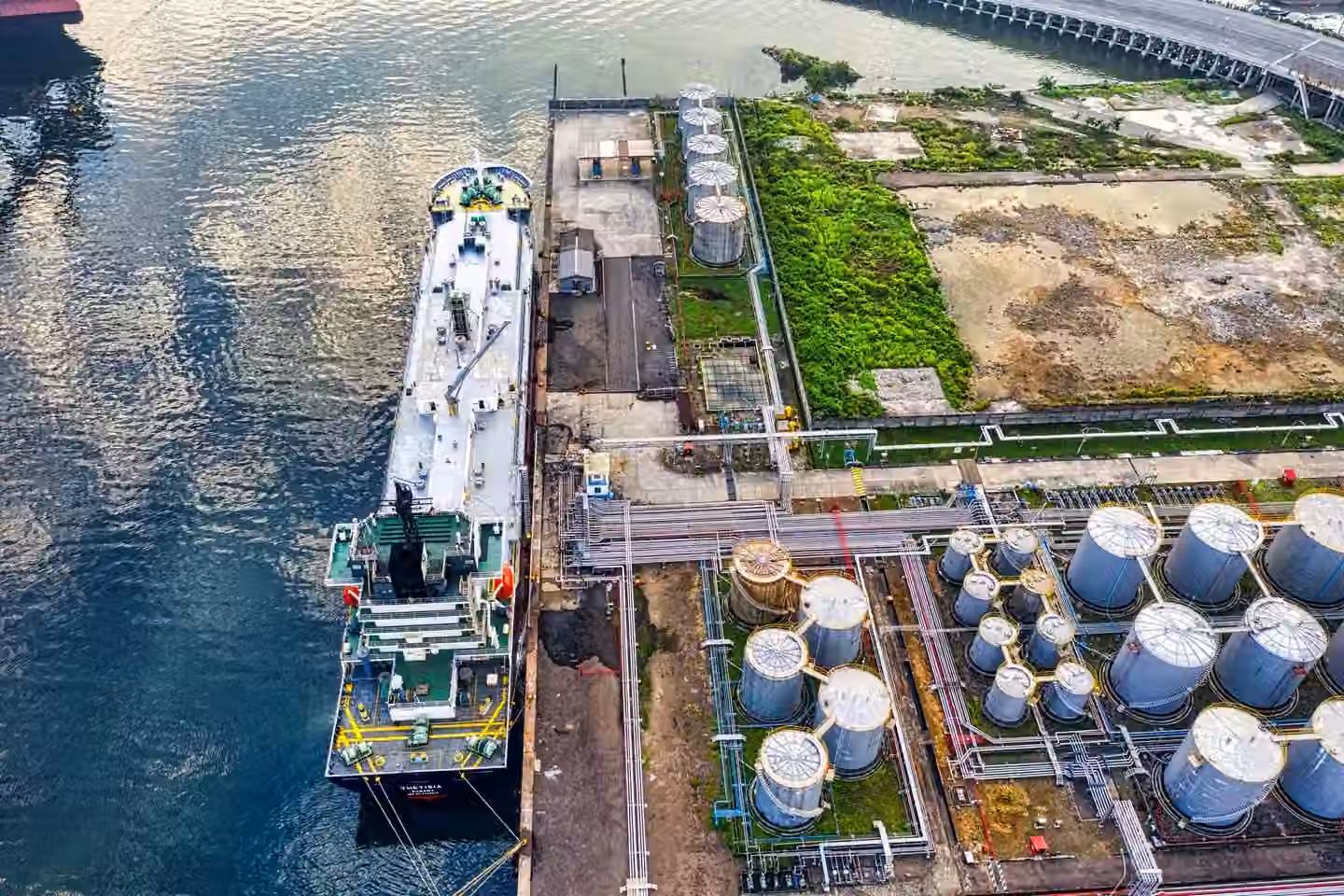 Aerial view of a ship docking at an industrial port with storage tanks in North Jakarta.