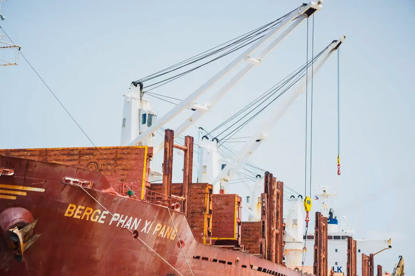 A large cargo ship named Berge Phan Xi Pang is docked, equipped with cranes for loading and unloading.