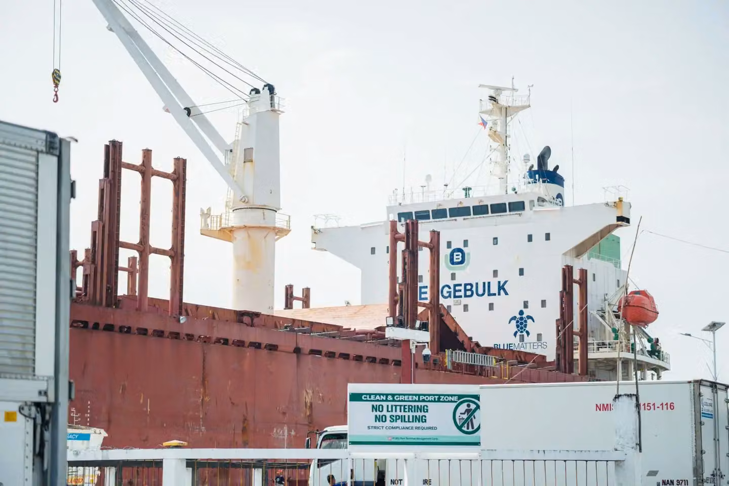 A cargo ship named Egebulk docked at a port, with cranes and containers visible.