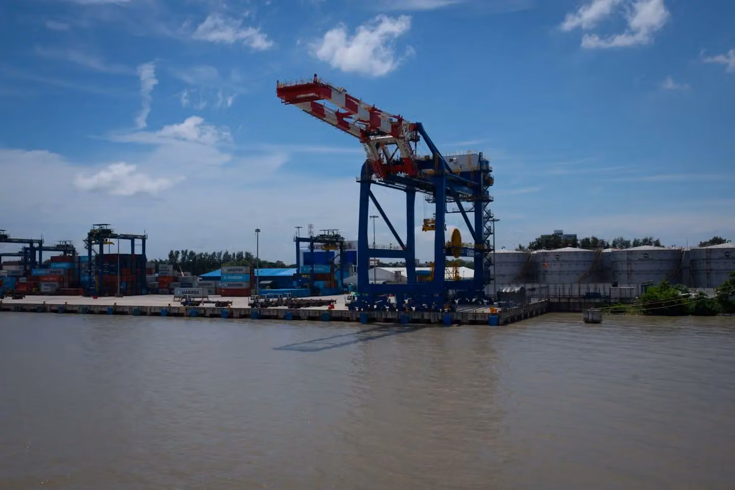 View of a busy industrial port with cargo cranes and containers under a clear blue sky.