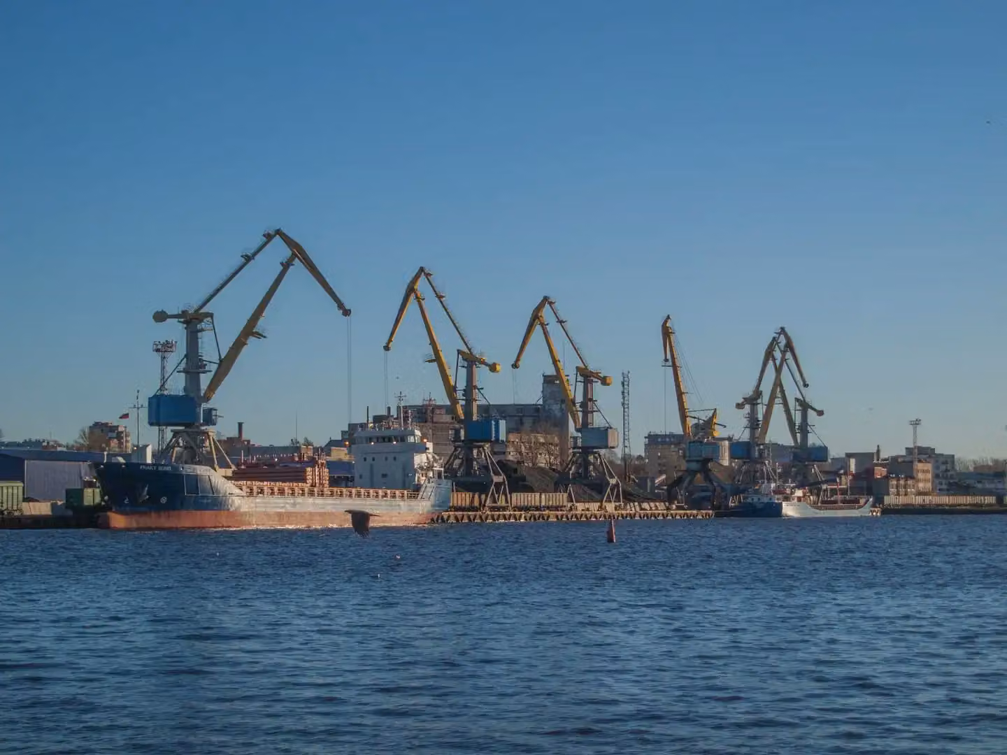 Image of an industrial shipyard with cranes and ships on a sunny day.