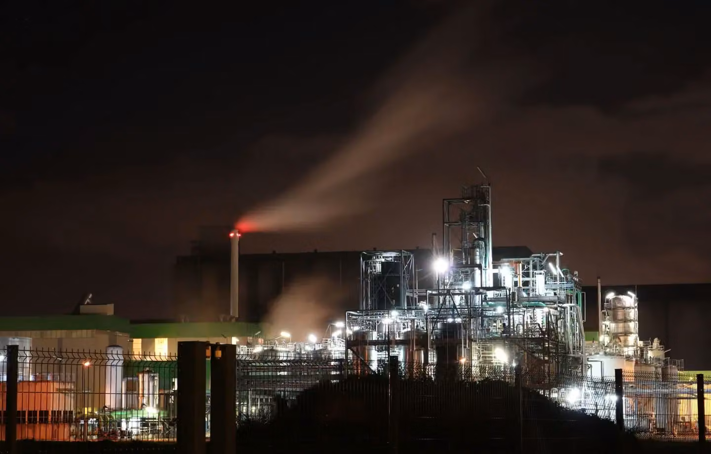 Illuminated refinery emitting smoke at night in Normandie, highlighting industrial impact.