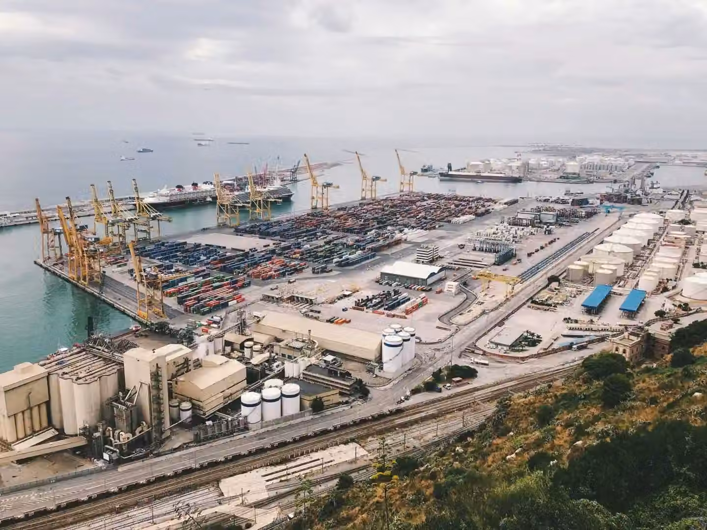 An aerial view of a busy industrial cargo port with cranes, containers, and ships.